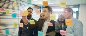 Team of young male professionals working through ideas on a glass board in a meeting room