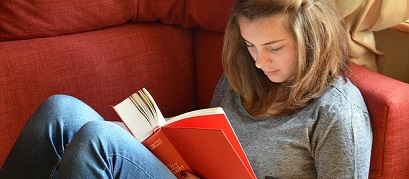 Young woman reading a book sat on a red sofa